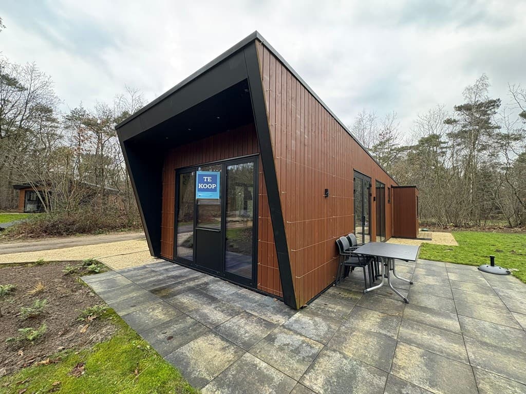 Moderne vakantiewoning met houten gevel, grote ramen en terras met tafel en stoelen in een bosrijke omgeving