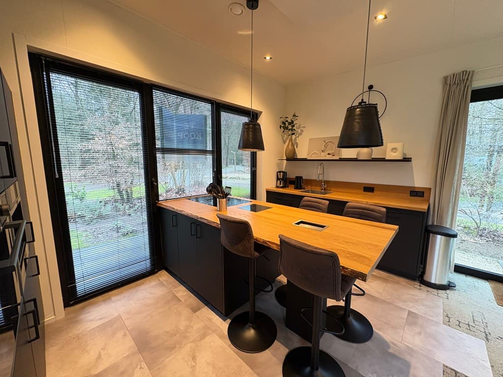 Moderne keuken met houten bar, hoge stoelen en grote ramen met zicht op de buitenruimte.