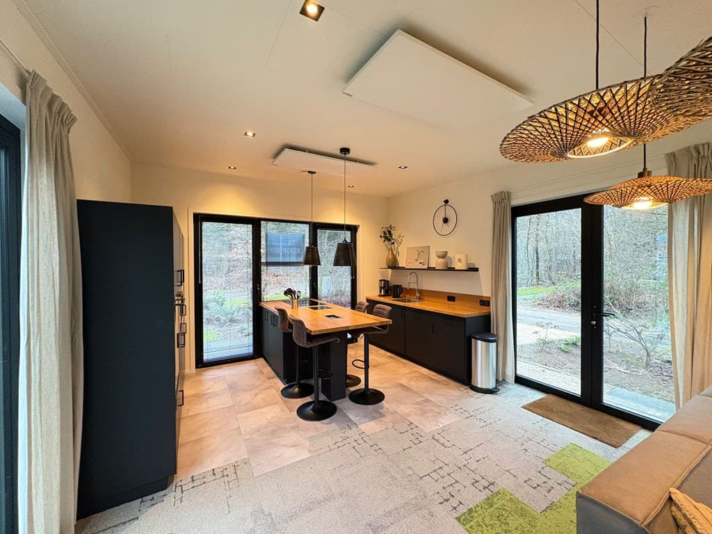 Moderne keuken met kookeiland, zwarte kastjes, grote ramen en natuurlijke lichtinval, gelegen in een rustige omgeving.
