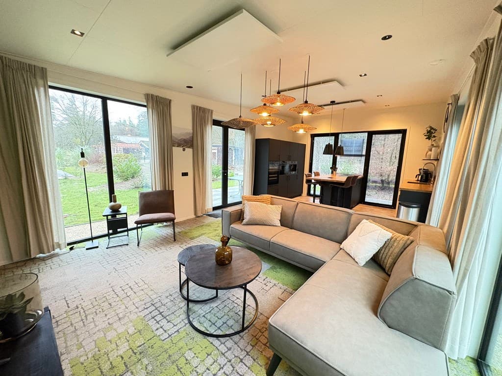Moderne woonkamer met bank, salontafel en grote ramen die uitzicht bieden op de tuin.