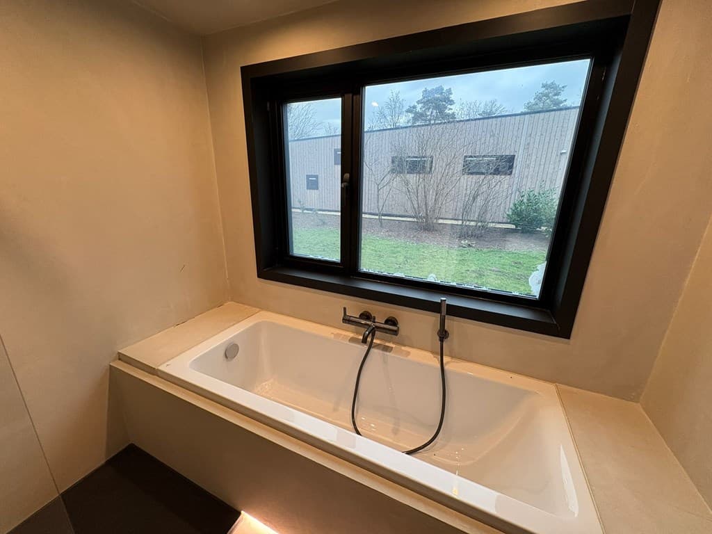 Licht badkamer met een ligbad naast een groot raam en uitzicht op de buitenruimte.