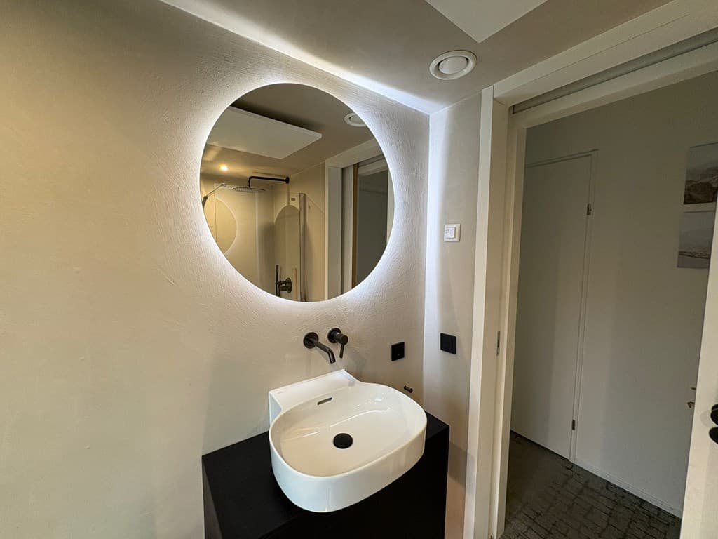 Moderne badkamer met ronde spiegel, wastafel en stijlvolle wandverlichting.