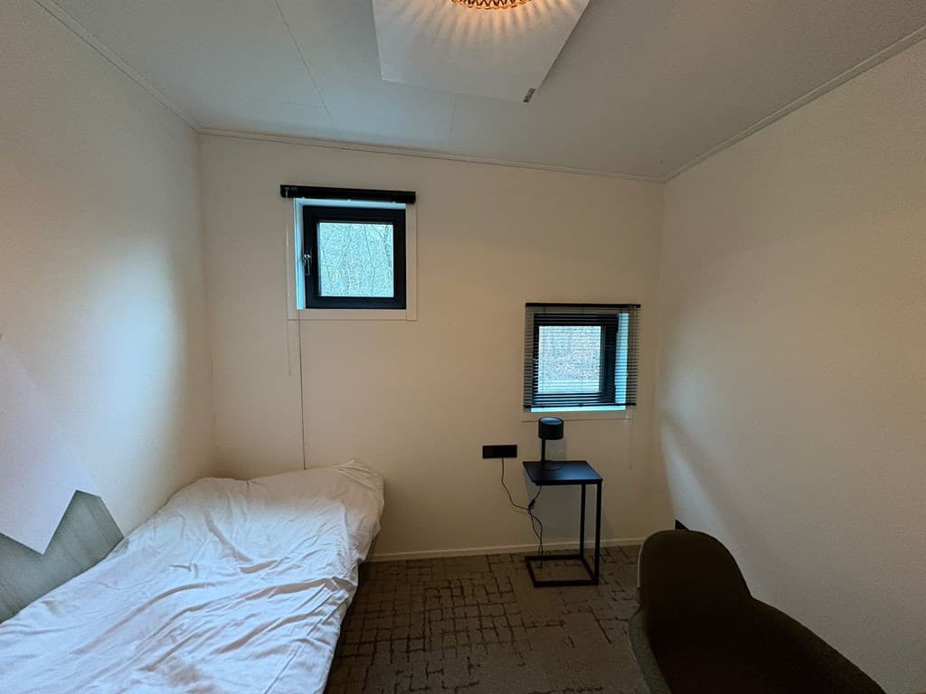 Kamer met een eenpersoonsbed, een stoel en twee ramen met uitzicht naar buiten