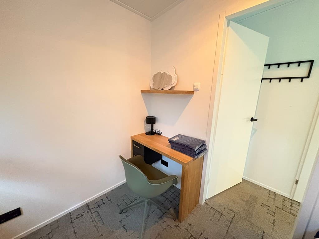 Kamer met bureau, stoel, wandplank en toegang tot een open deur naar een andere ruimte