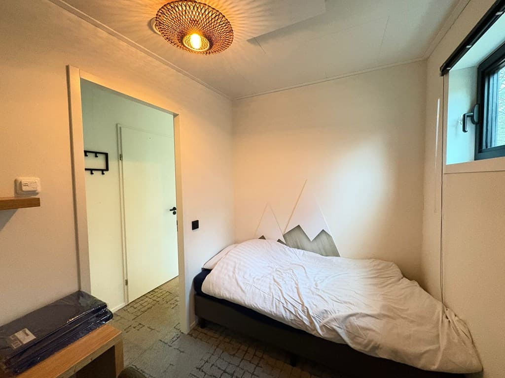 Slaapkamer met een eenpersoonsbed, een wand met bergmotief en een raam met zicht op buiten.