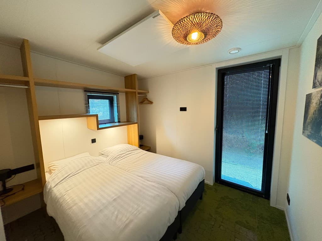 Slaapkamer met twee eenpersoonsbedden, houten meubels en een groot raam met jaloezieën.