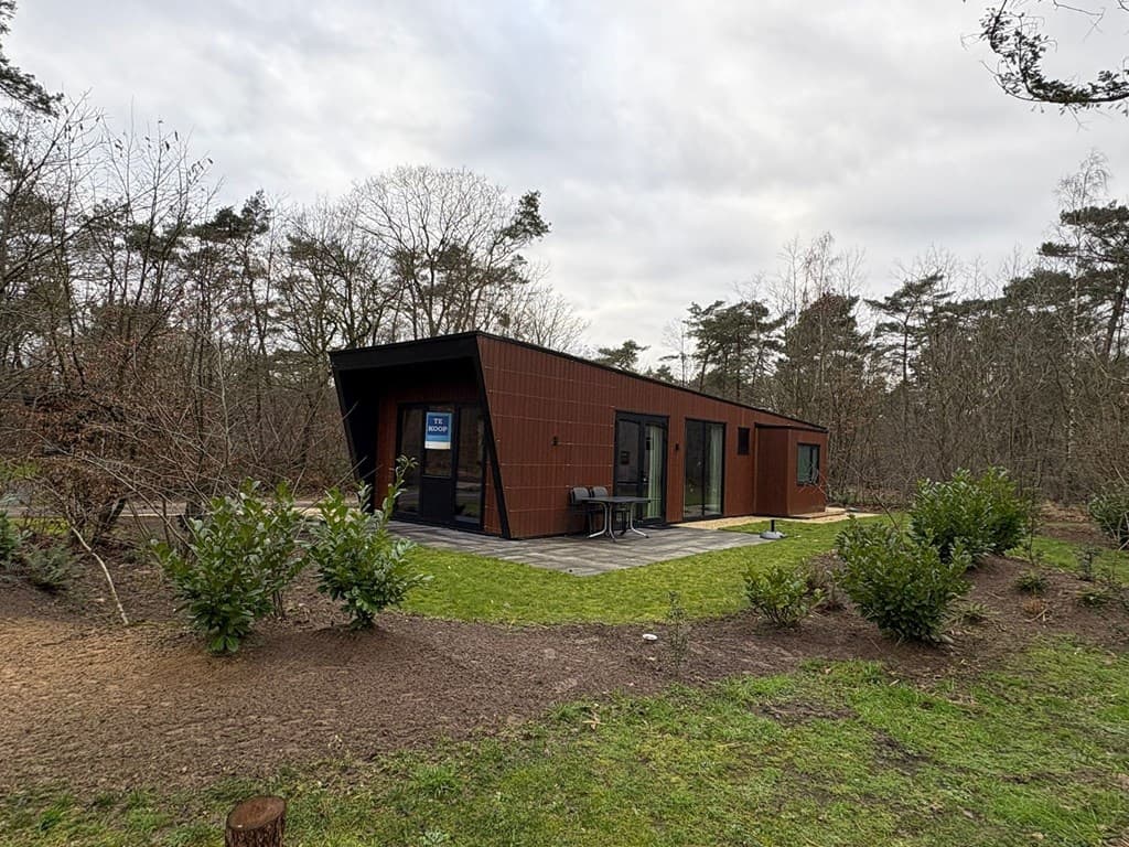 Moderne vakantiewoning met een houten gevel, gelegen in een bosrijke omgeving met een tuin en terras.
