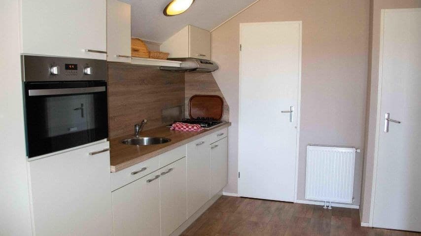 Moderne keuken met oven, kookplaat, spoelbak en opbergkasten in lichte kleuren.
