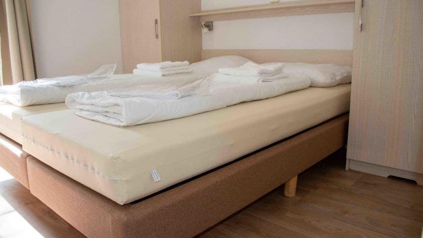 Slaapkamer met een tweepersoonsbed, kledingkast en stapels schone handdoeken op bed.