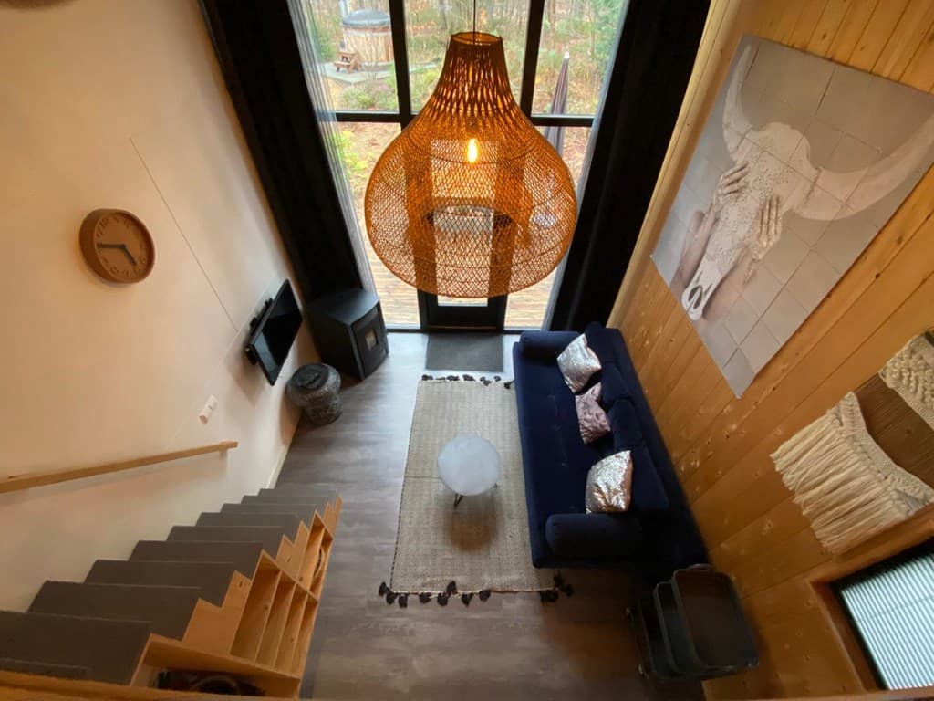 Huiselijk interieur met een blauwe bank, een ronde tafel en een grote hanglamp bij een raam met uitzicht op de buitenruimte.
