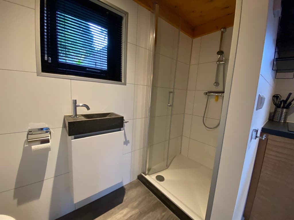 Moderne badkamer met douche, wastafel en venster met vensterdecoratie in EuroParcs Beekbergen.