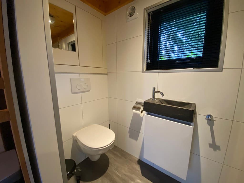 Toiletruimte met modern wastafeltje, toilet en een spiegel aan de wand, voorzien van lichte tegels en houten plafond.