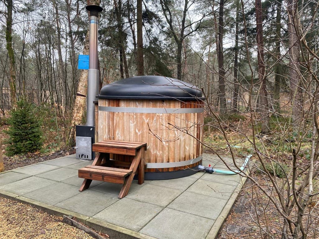 Houten hottub op een betegeld terras, omringd door bomen en natuur in EuroParcs Beekbergen.