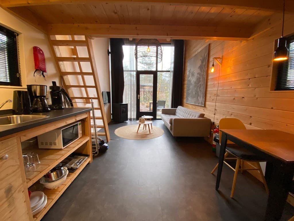 Huiselijke woonkamer met open keuken en trap naar de bovenverdieping, veel natuurlijk licht en houten afwerking