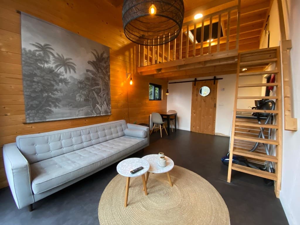 Houten interieur met een zithoek, trap naar een vide en een eetgedeelte met een tafel en stoelen.