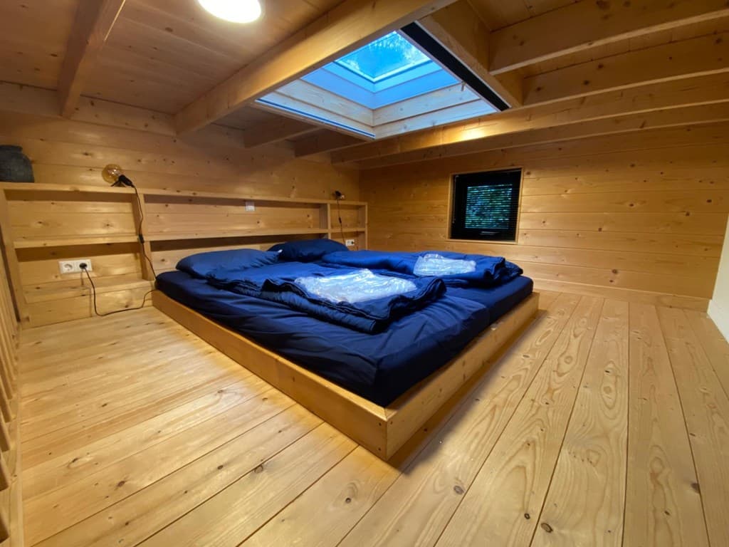 Slaapkamer met houten wanden, een dakraam en een tweepersoonsbed met een blauwe dekbedset.