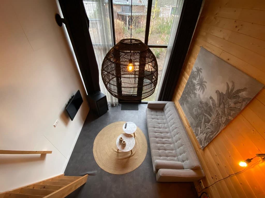 Zicht op de woonkamer met een grijze bank, ronde tafel, grote lamp en kunst aan de muur.