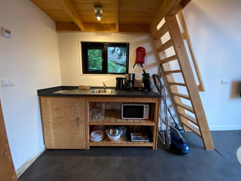 Keukenruimte met houten kast, aanrecht, kookplaat, magnetron, en trap naar boven.