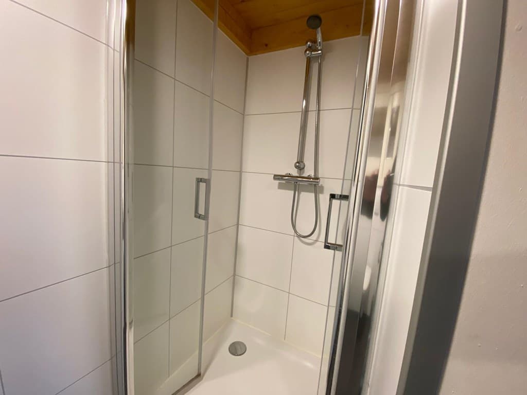 Moderne douchecabine met glazen wanden en tegelwand in lichte kleurstelling.