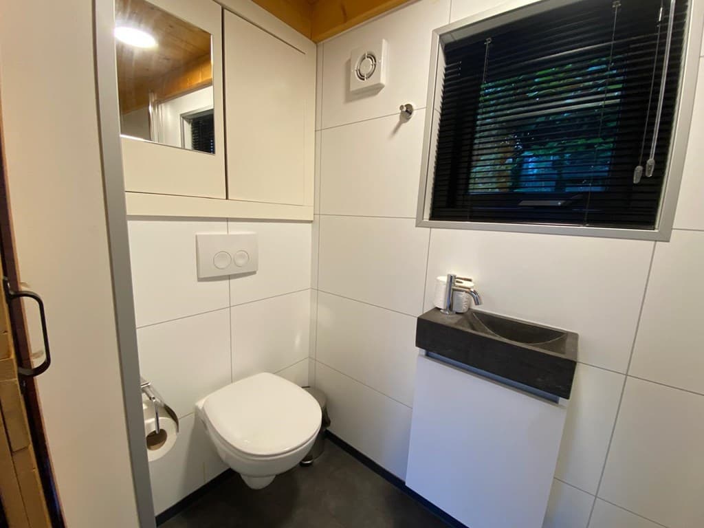 Moderne badkamer met toilet, wastafel en spiegel, voorzien van witte en donkere wandtegels.