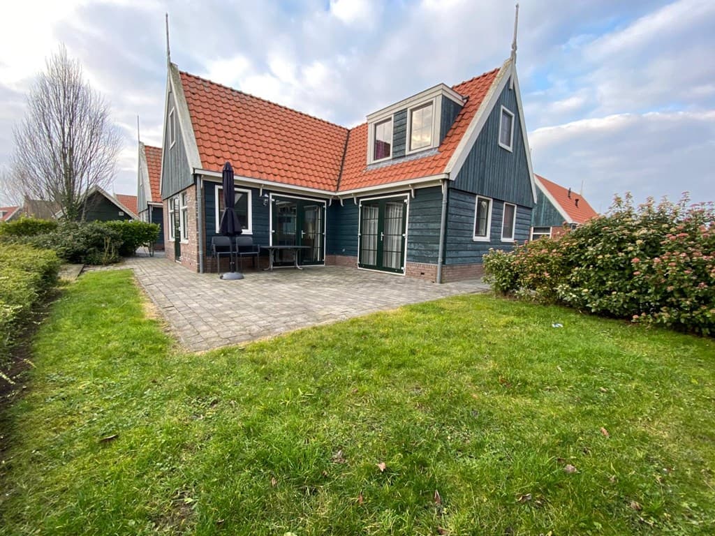 Groene tuin met bestrating en een vakantiehuis van twee verdiepingen met rode dakpannen en een overdekt terras