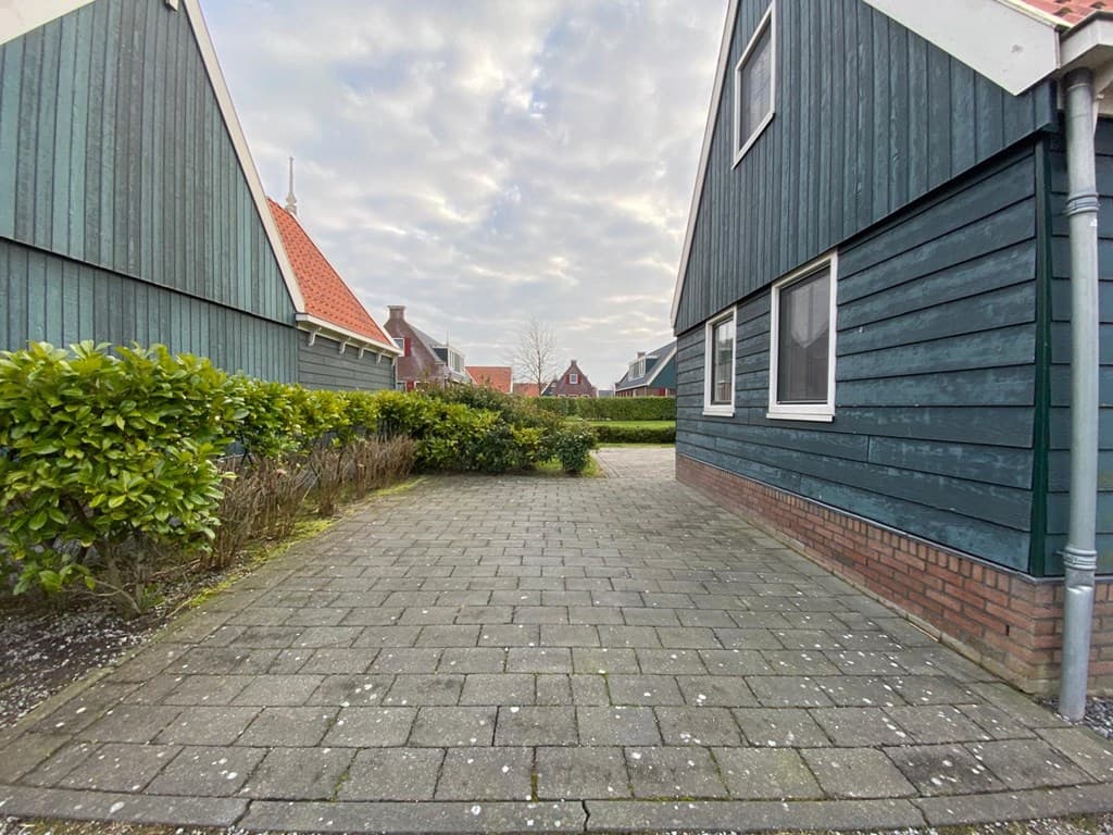 Tegeltuin met groene busjes tussen twee woningen en een doorkijkje naar de straat achteraan