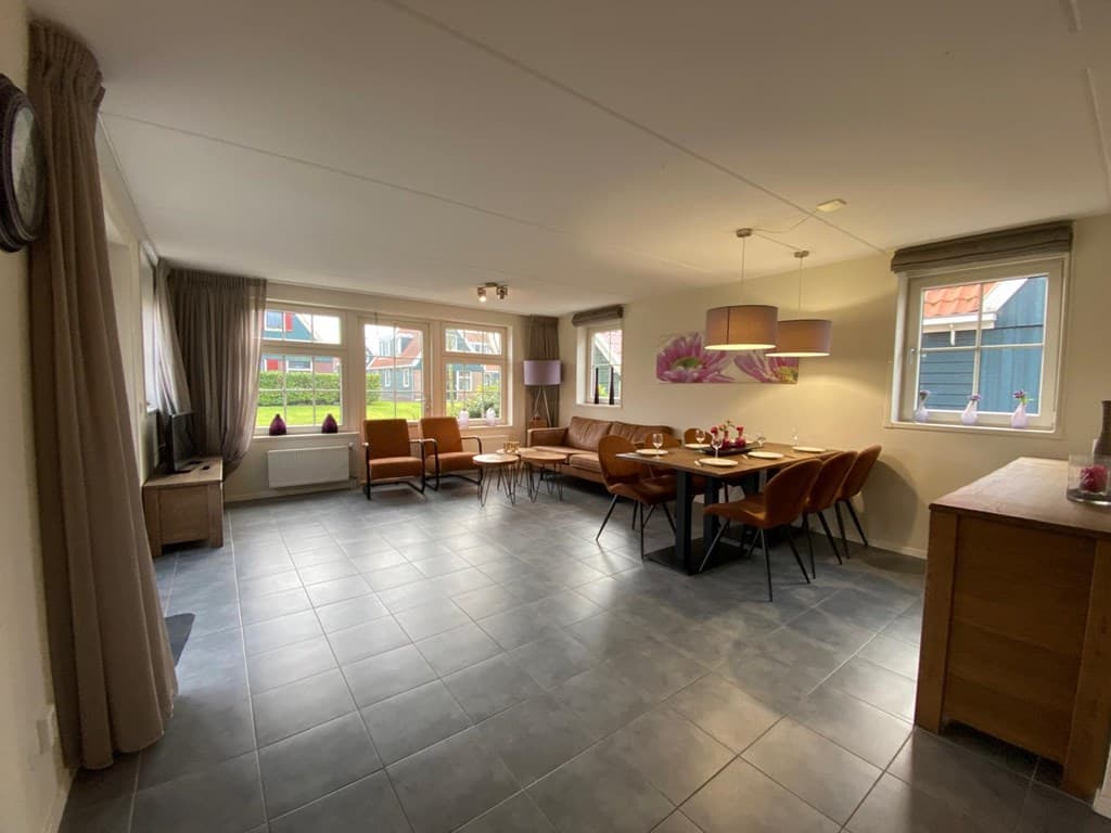 Ruime woonruimte met grote ramen, zithoek, eettafel en moderne inrichting, voorzien van neutrale kleuren en lichte meubels