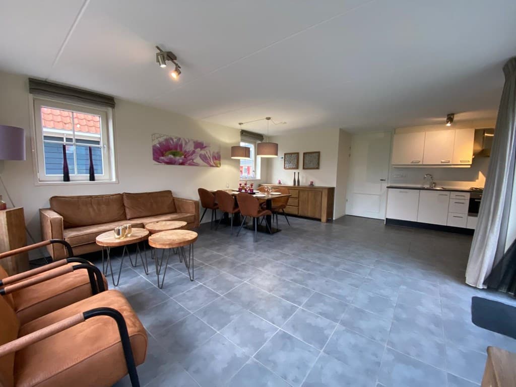 Ruime woonkamer met zithoek, eettafel en open keuken, voorzien van tegels en moderne inrichting.