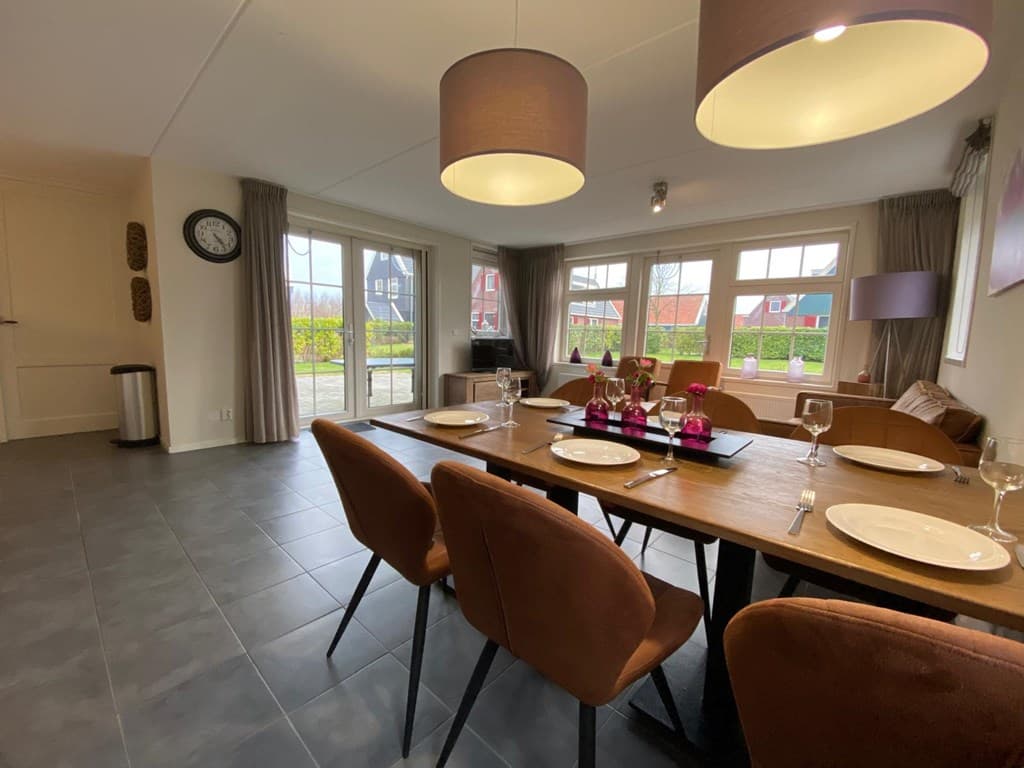 Eetkamer met lange tafel, stoelen, grote ramen en uitzicht op de tuin, moderne verlichting en neutrale kleuren