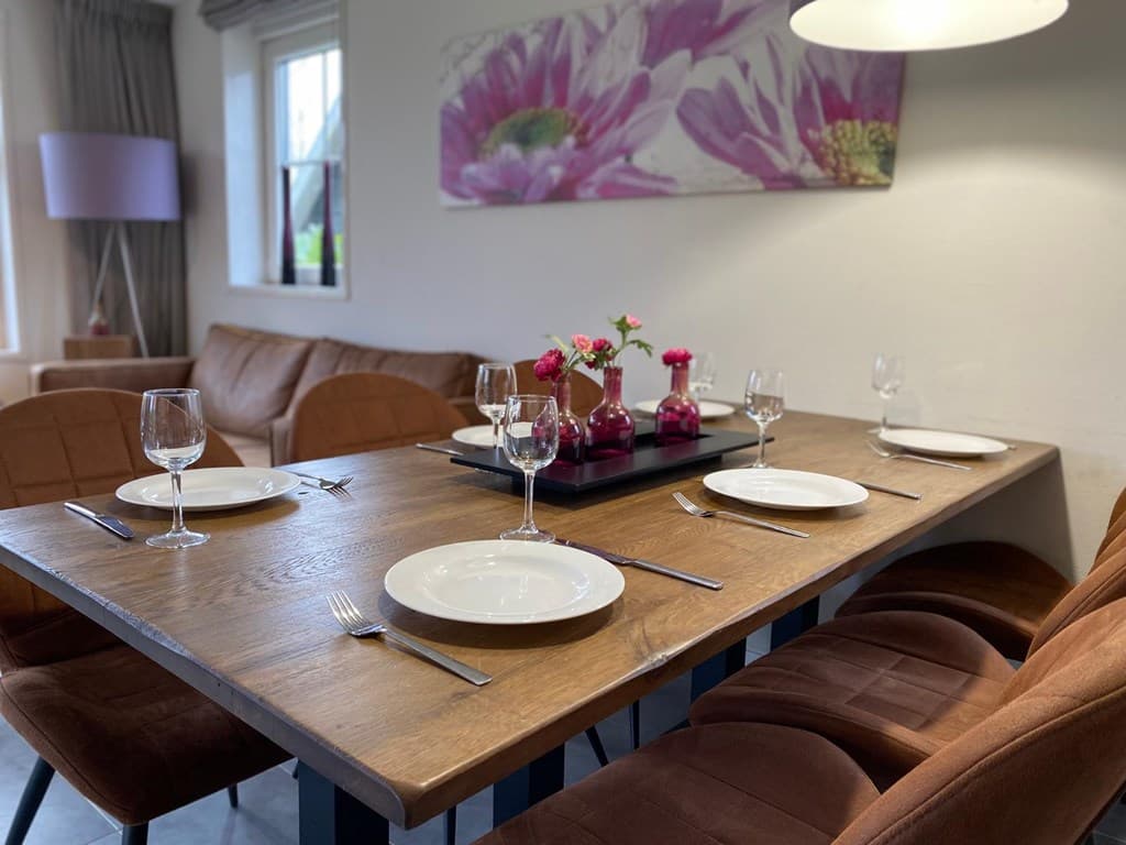 Eetkamer met een houten tafel, vier stoelen en een bloemstuk op tafel, kunst aan de muur en natuurlijk licht vanuit het raam