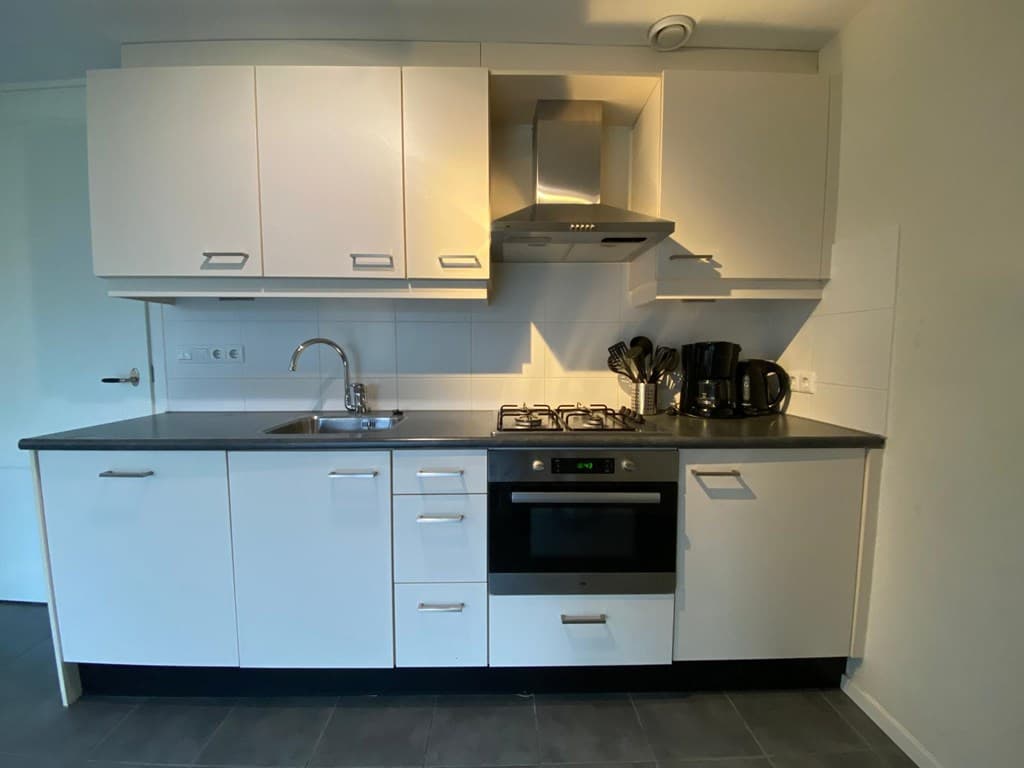 Moderne keuken met witte kasten, gasfornuis, stainless steel afzuigkap en diverse keukenapparaten.