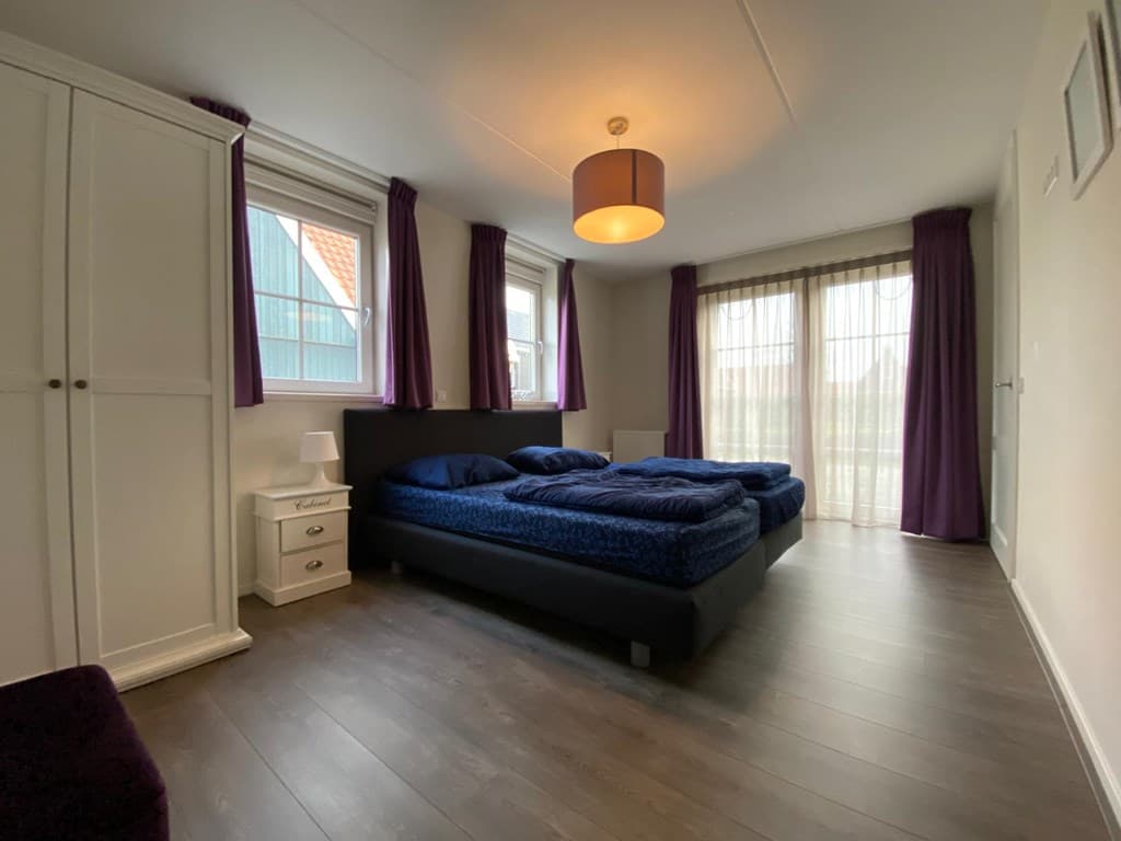 Slaapkamer met twee eenpersoonsbedden, witte kast, nachtkastje en grote ramen met gordijnen