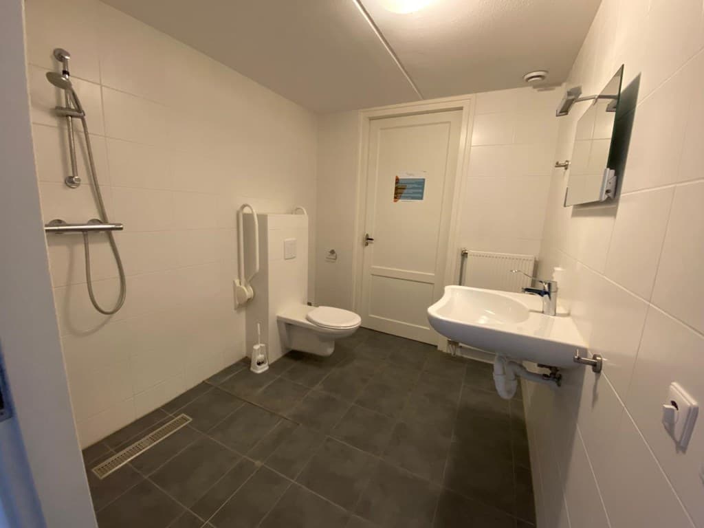 Ruime, betegelde badkamer met een douche, toilet en wastafel, voorzien van een spiegel en handdoekhouder