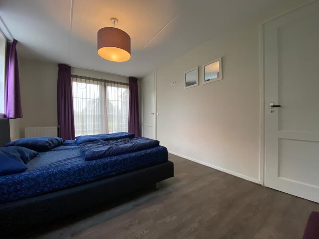 Slaapkamer met twee eenpersoonsbedden, ramen met paarse gordijnen en een deur naar een andere ruimte