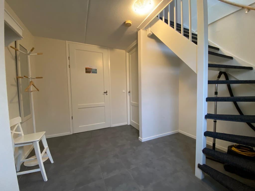 Ingang van een vakantiewoning met een open hal, trappenhuis en een zitje met een kapstok aan de muur
