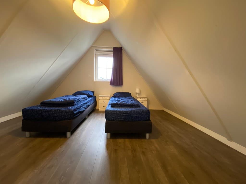 Slaapkamer met twee aparte eenpersoonsbedden, houten vloer en een raam met uitzicht naar buiten