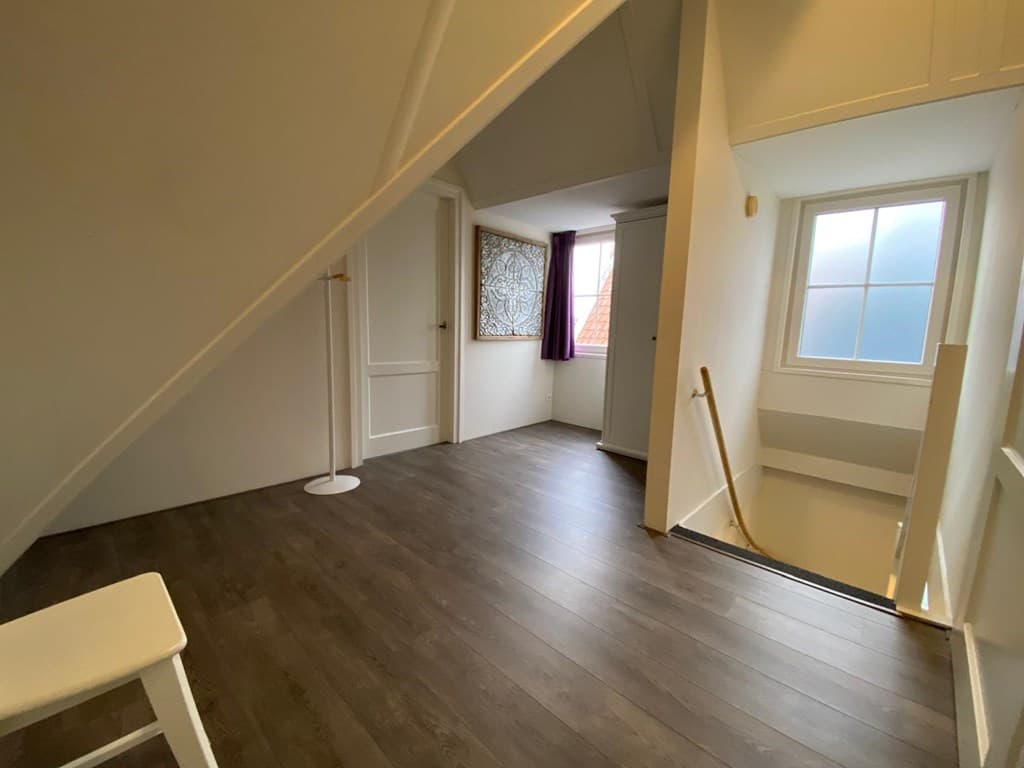 Ruime traphal met een houten vloer, venster met zicht naar buiten en een trap naar de onderverdieping