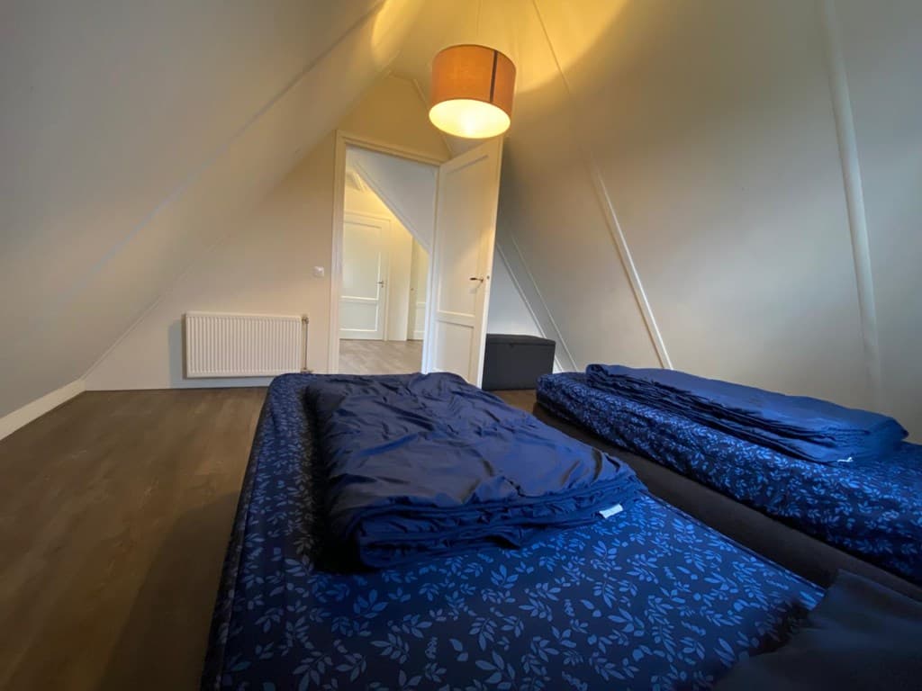 Slaapkamer met twee enkele bedden, plafond met lamp en deur naar een andere ruimte, wanden in lichte kleur