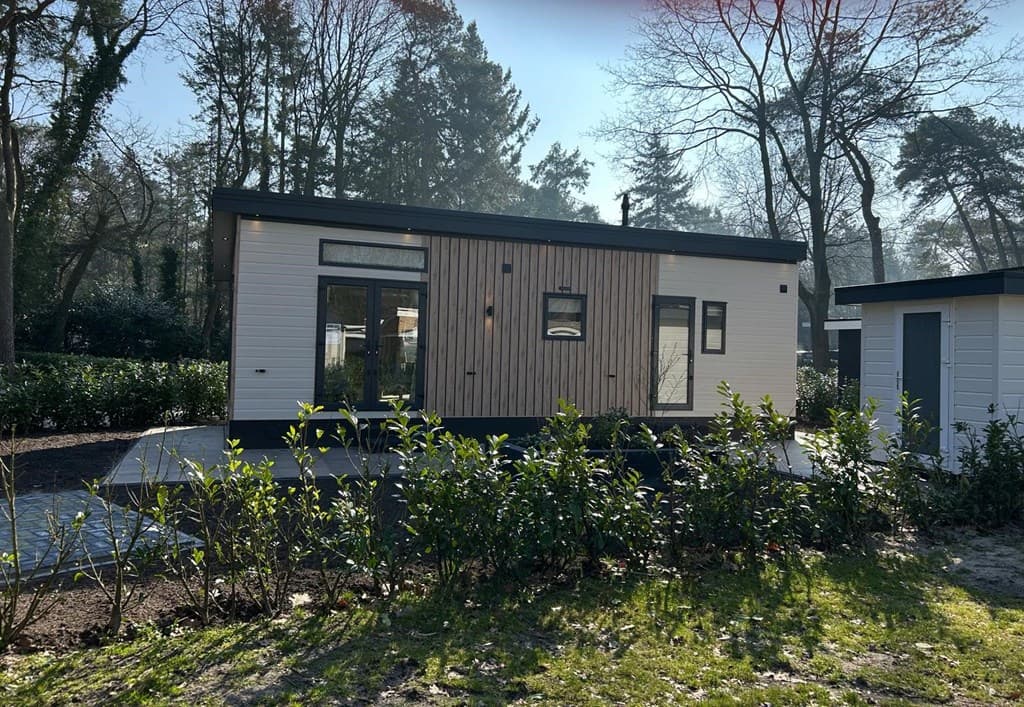 Moderne vakantiewoning met houten gevel en grote ramen, omringd door bomen en struiken op Camping De Konijnenberg