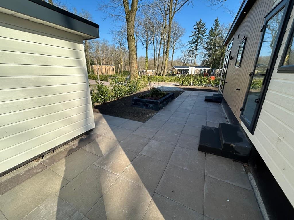 Buitenaanzicht van een woning met betegeld terras en plantenbed in een groene omgeving met bomen in Harderwijk.