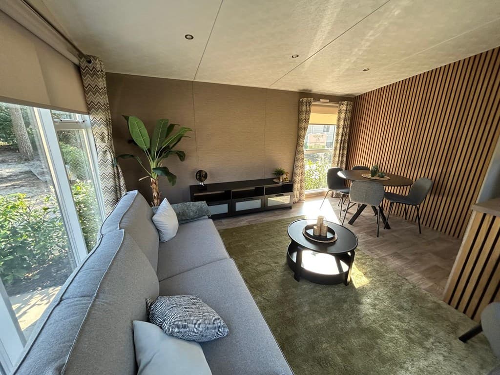 Ruime woonkamer met een grijze bank, ronde tafel en moderne decoratie in Camping De Konijnenberg, Harderwijk