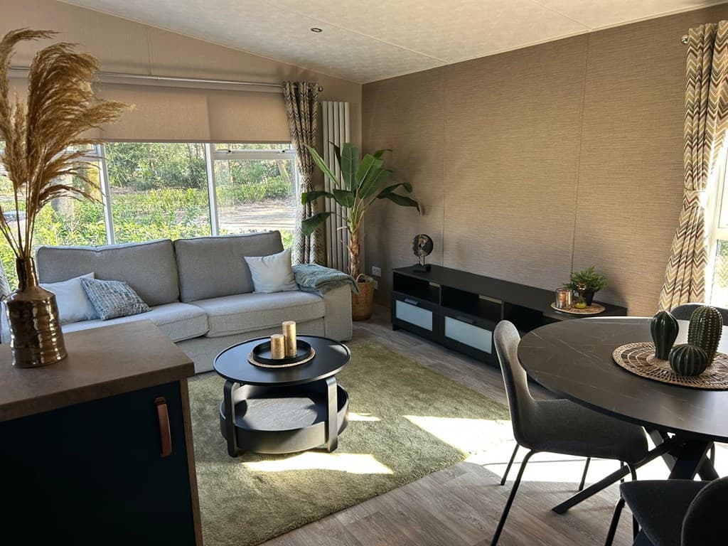 Modern ingericht woongedeelte met een bank, planten en een eettafel bij een groot raam met uitzicht op groen.