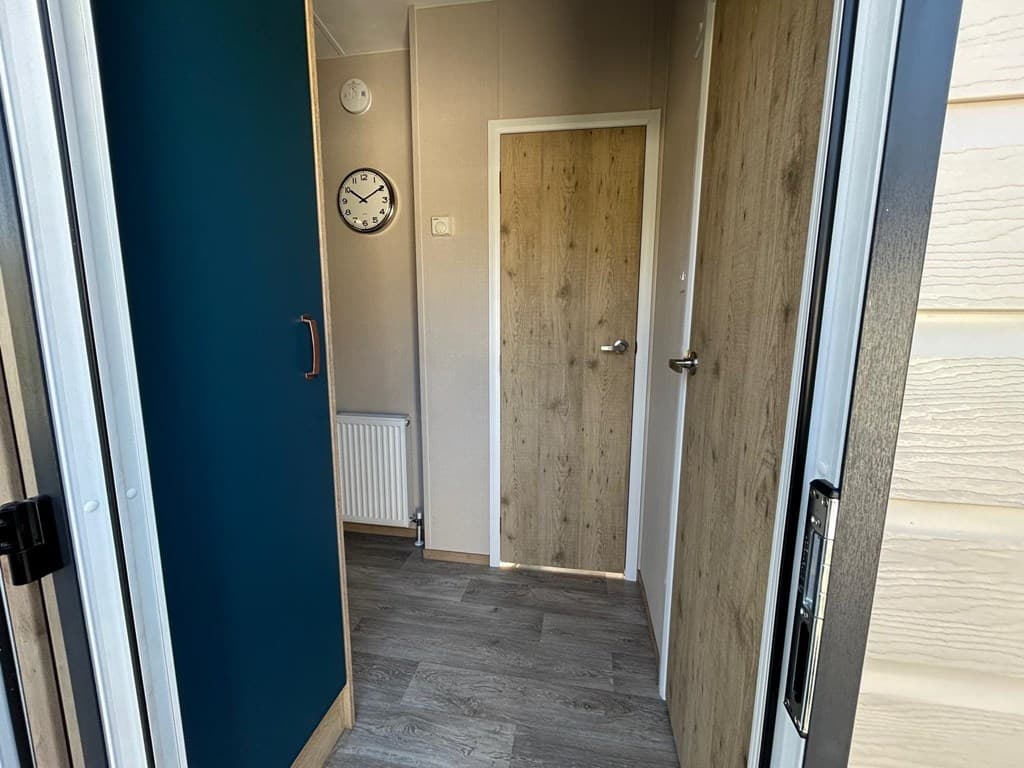 Entree van de vakantiewoning met een deur, klok en houtlook afwerking op de muren en vloer.