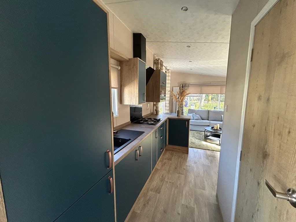 Moderne keuken met blauwe kasten, kookplaat en toegang tot een lichte woonkamer met grote ramen.