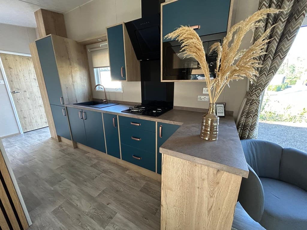 Hedendaagse keuken met blauwe kasten, gasfornuis en een comfortabele zithoek met een plantenstuk.
