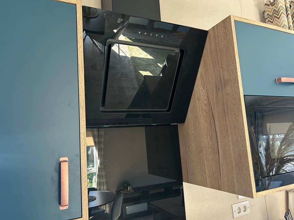 Keuken met moderne kastjes in blauw en hout, met een inbouwoven en een tafel zichtbaar op de achtergrond.