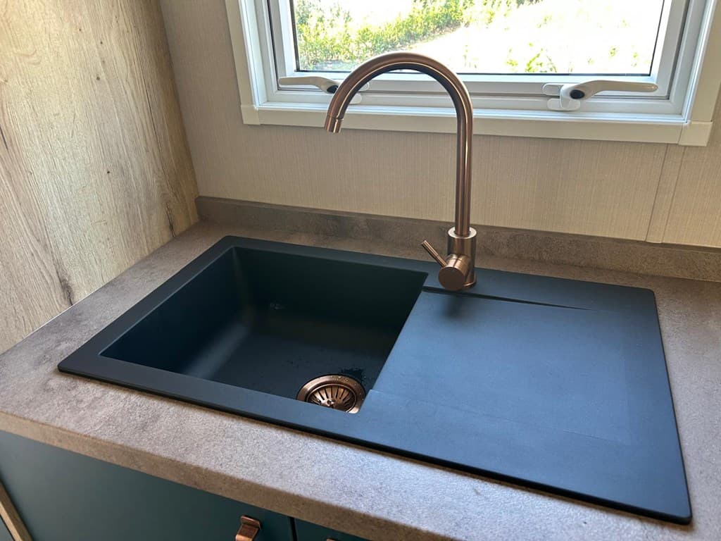 Zwarte spoelbak met moderne kraan, ingebouwd in een werkblad naast een raam met zicht naar buiten.