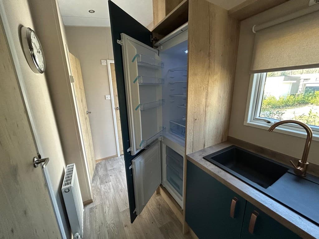 Keuken met open koelkast en zwarte spoelbak, lichte muren en houten accenten in de woning op Camping De Konijnenberg.