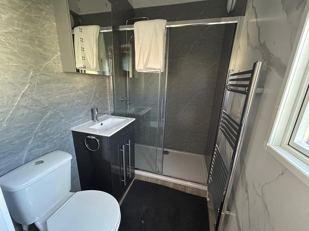 Moderne badkamer met douche, toilet en wastafel in strakke afwerking en grijze tegels.