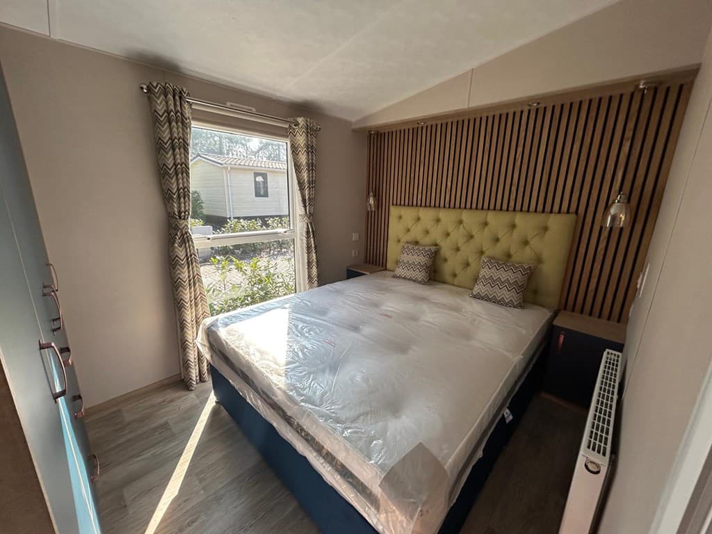 Slaapkamer met een groot bed, gestoffeerde hoofdbord en ramen met zicht op de buitenomgeving.